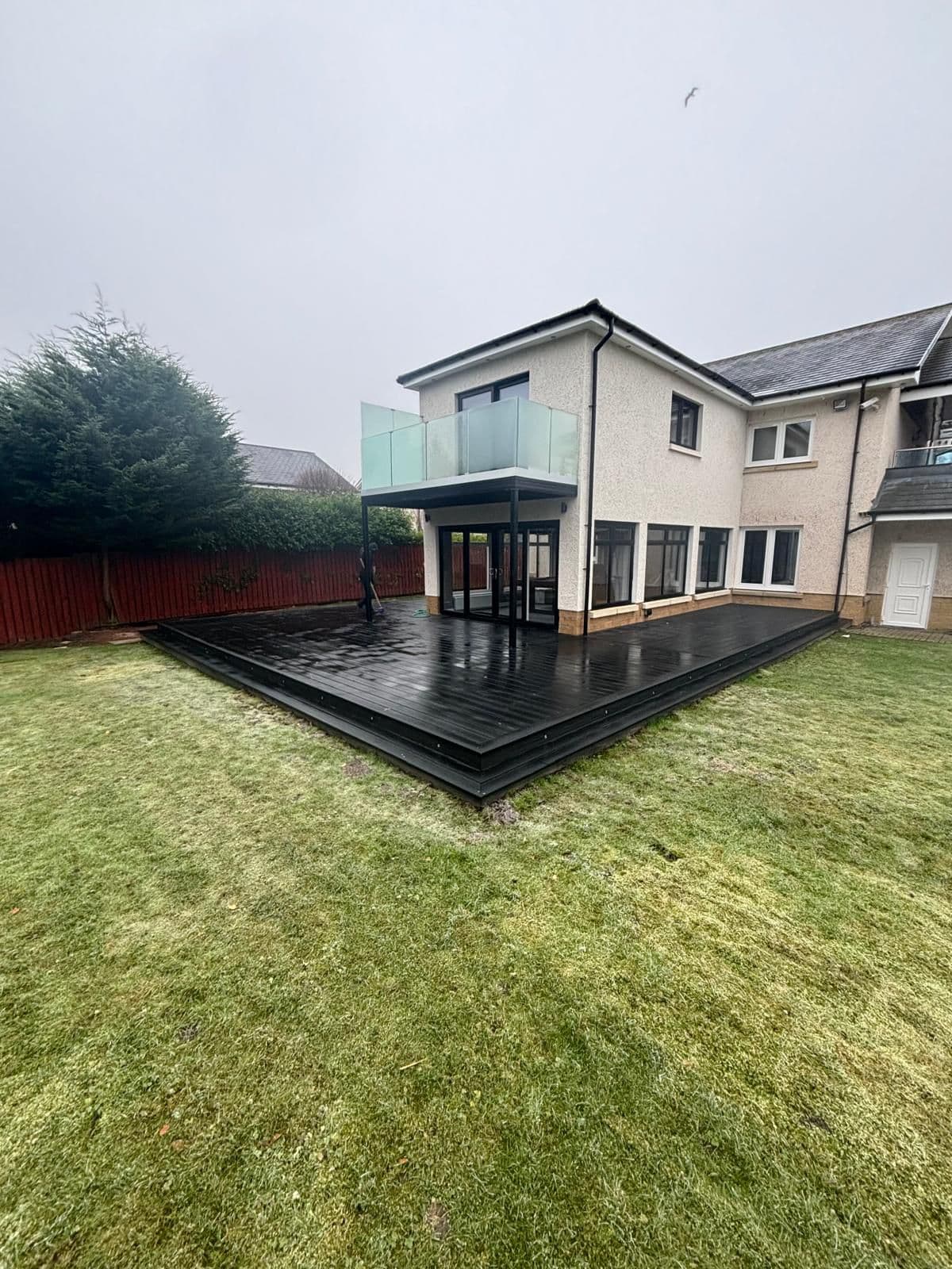 Black composite decking wrapping a two-storey house with glass balustrade balcony