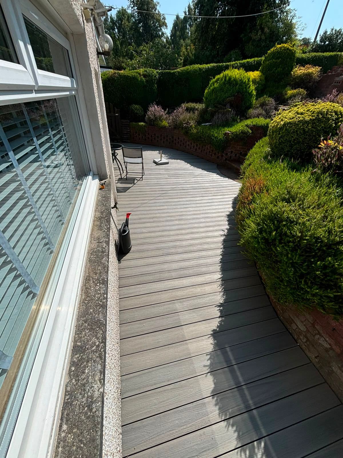Curved grey composite decking path through a landscaped garden
