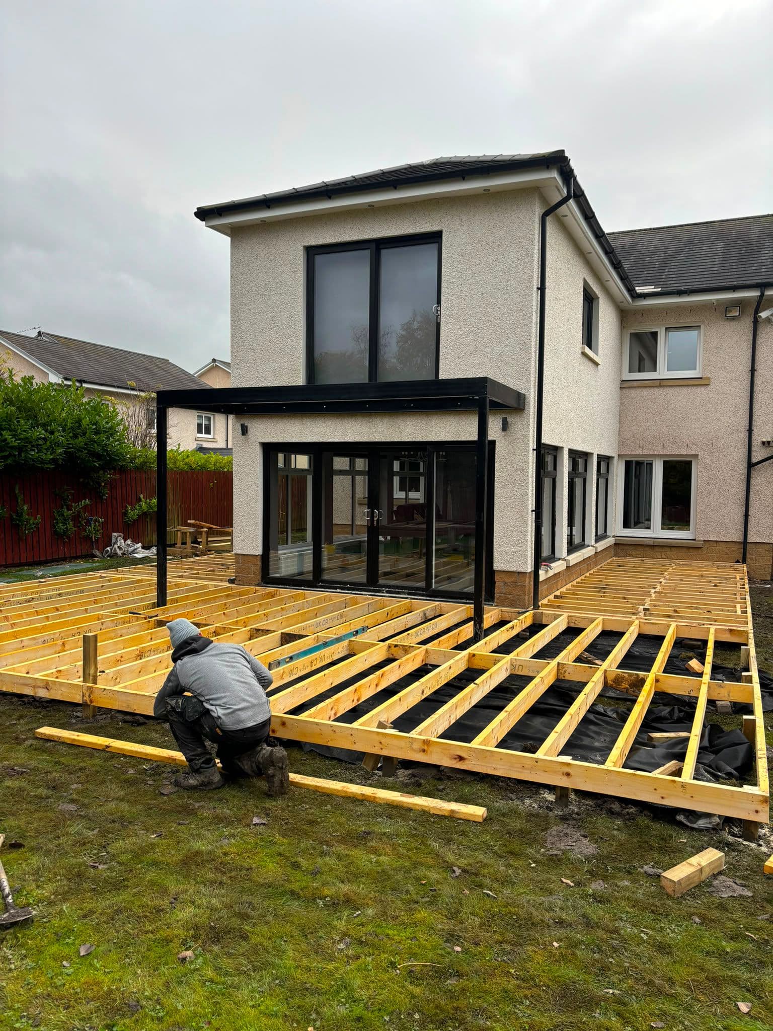 Deck sub-frame being built beneath a rear house extension with glass balcony
